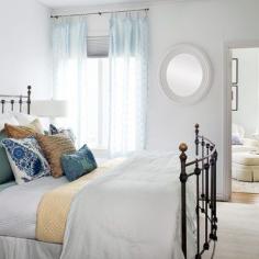 Rich golds, ethereal blues, and acres of white create a dreamy bedroom scene while a graphic black-iron bed keeps the bedroom grounded. | Photo: Ken Gutmaker | thisoldhouse.com