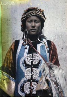 China | A young Yongning woman poses in large earrings and embroidered robe. Yunnan Province. ca. July 1931 | © Dr. Joseph F. Rock/National Geographic Society/Corbis