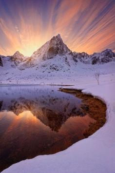 
                    
                        The northern lights and beautiful landscapes in Sweden and Norway - Rays of sunlight streak over a snowy peak reflected in a lake in Lofoten Islands, Norway
                    
                